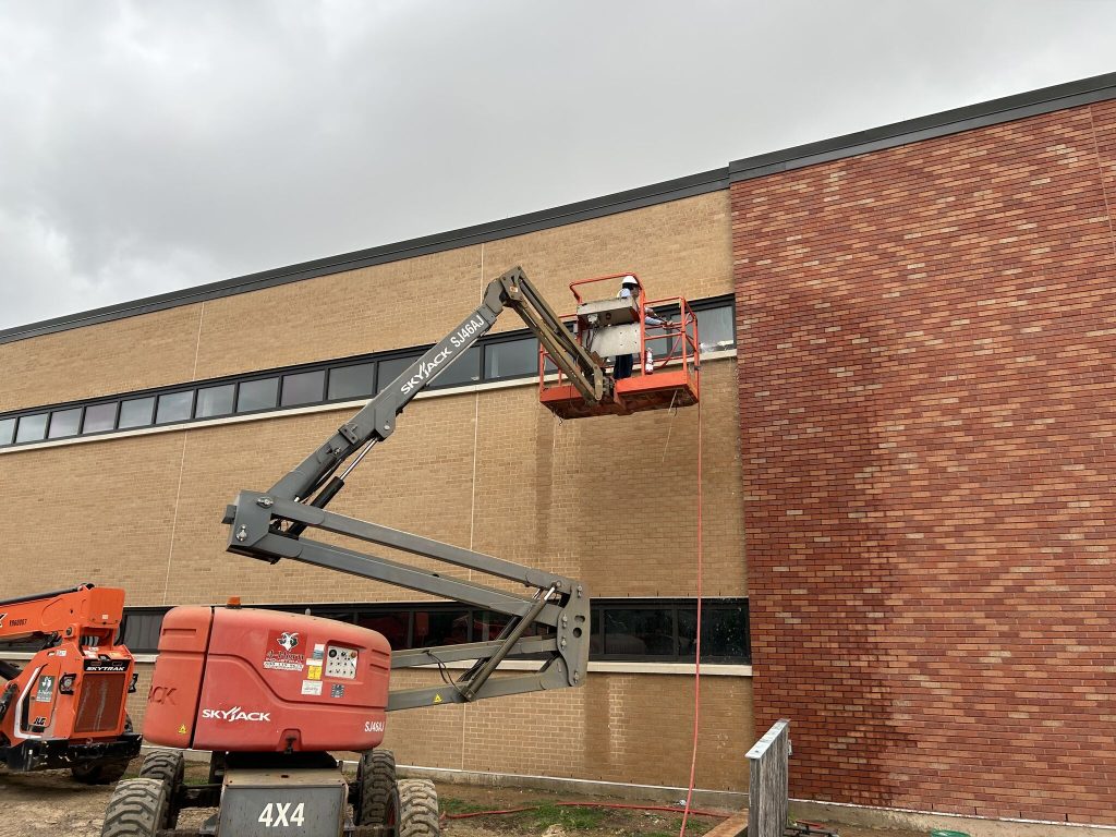 Technician performing ASTM E1105 chamber testing on a building window at Lamar University, spraying water to simulate wind-driven rain.